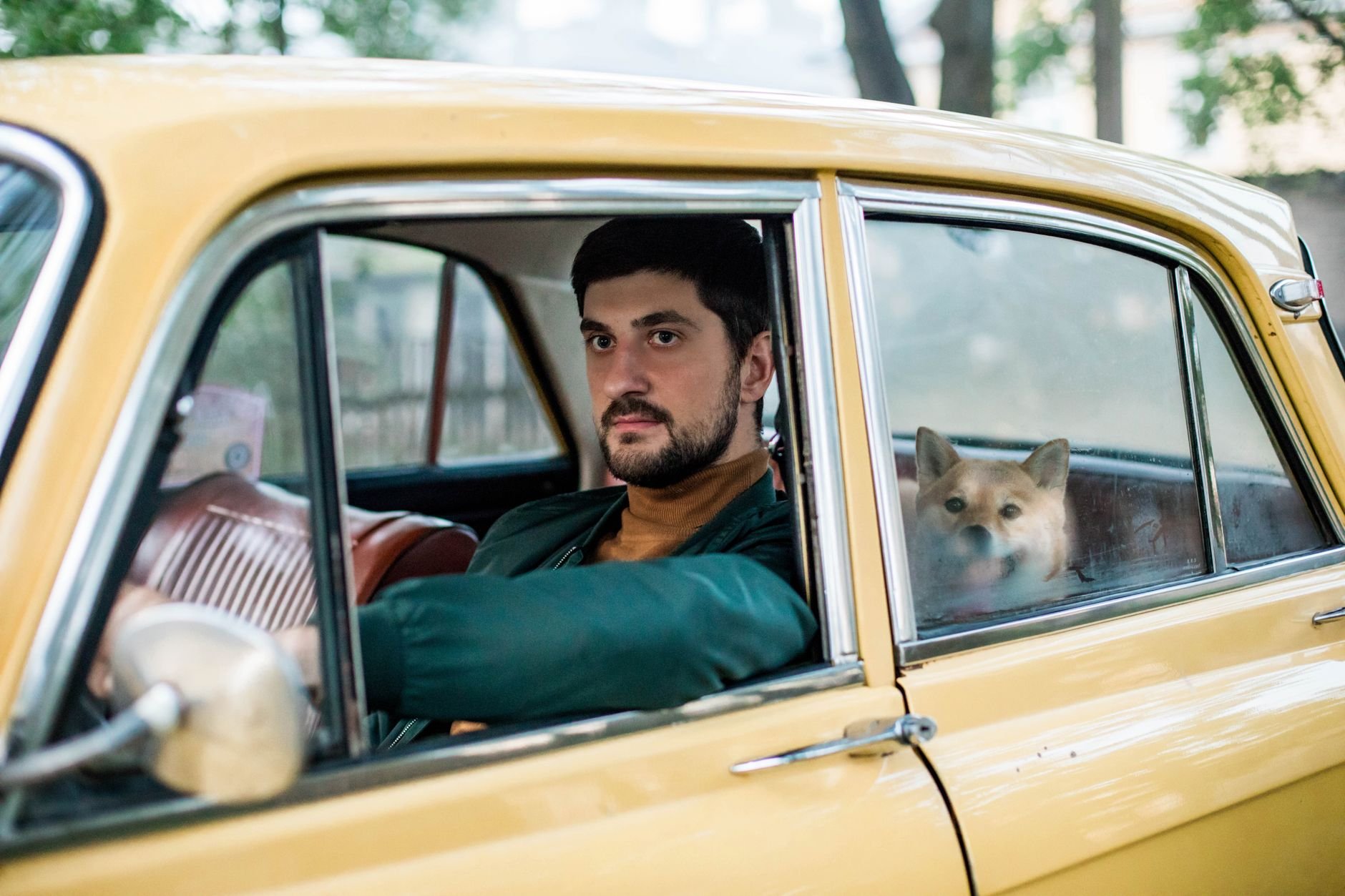 Man driving with a dog safely in the back seat of his vehicle.